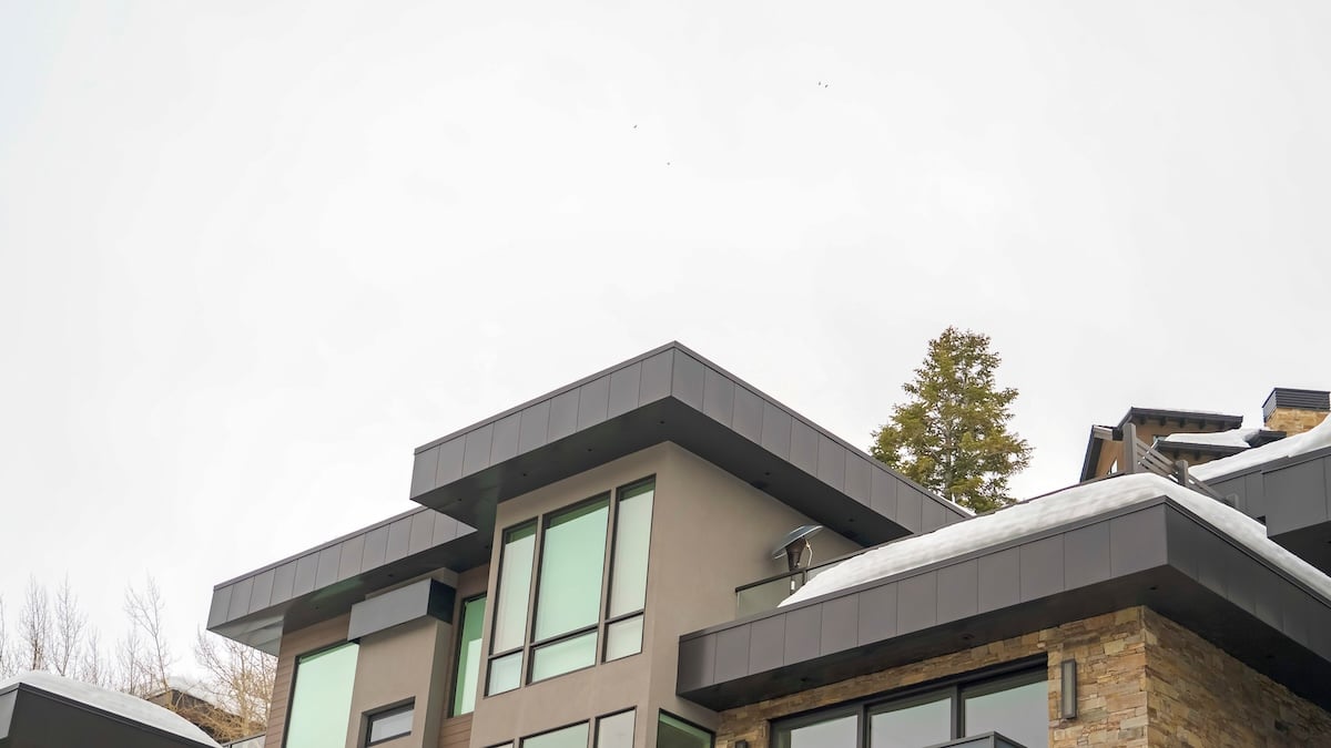 Panorama Modern home exterior with stone wall and flat roof against white sky in winter. The snowy house also features an outdoor stairs and balconies.