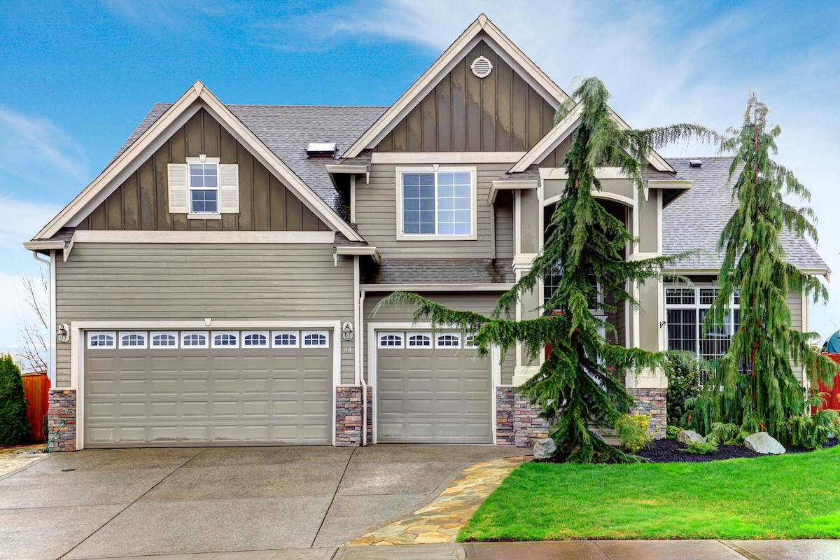 Beautiful olive siding house with tile roof, columns stoned at base, garage and green front trim