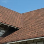 Brown asphalt shingled roof valley leaking problem area with a ventilation cap. A close-up of asphalt shingles installed on a roof valley with a waterproof flashing. Asphalt shingles roofing.