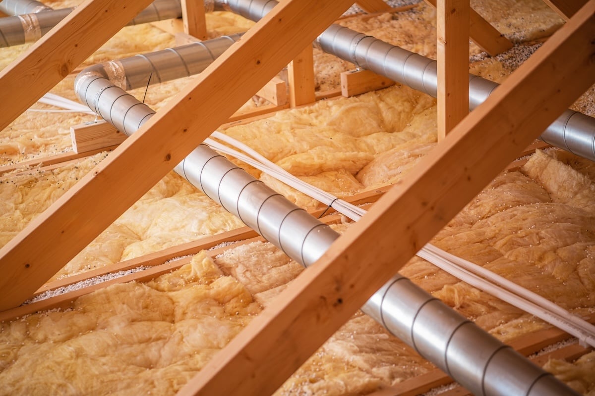 roof insulation Wooden beams support a network of pipes and ductwork, showcasing insulation materials in a residential attic during ongoing construction activities.