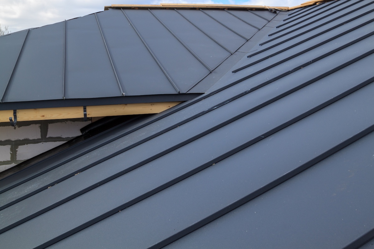 metal roof installation close up view of house under construction with grey folding roof on waterproofing layer