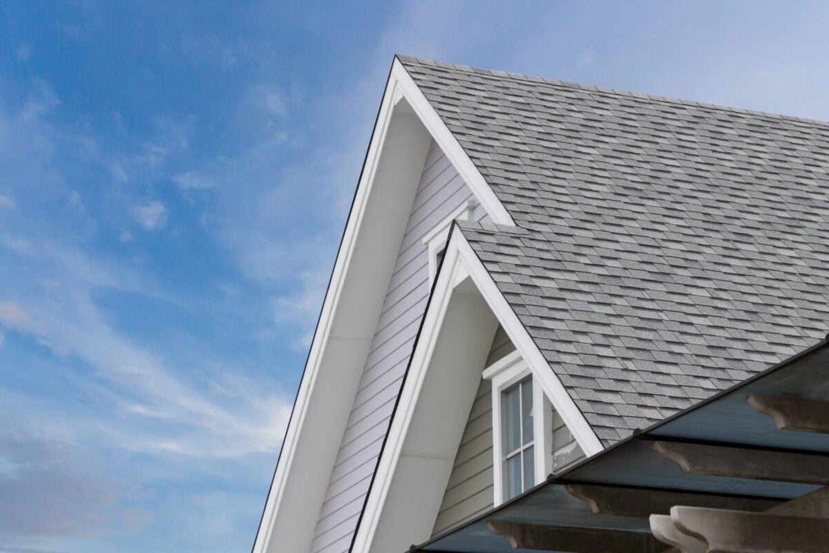 architectural shingles Roof shingles on top of the house against blue sky with cloud, dark asphalt tiles on the roof background.