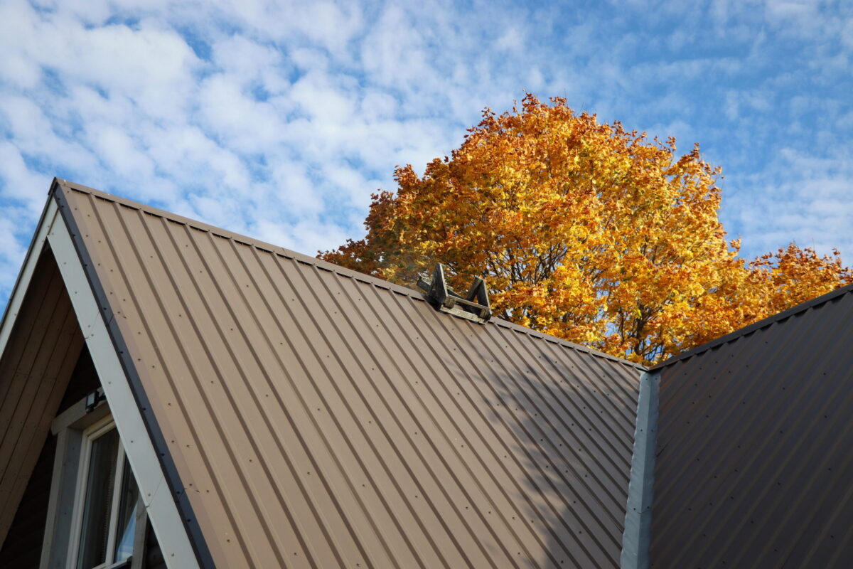 how long do metal roofs last Brown metalic roof house under the autmn tree against blue sky .