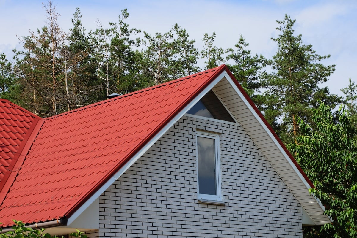 can you paint a metal roof gray brick attic with a window under a red tile roof against the sky and pine trees