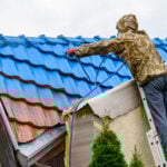 Professional painting old roof in blue color diligently. Work at heights.