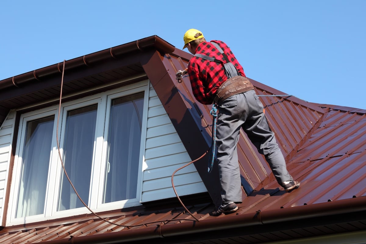 roofer builder worker with pulverizer spraying paint on metal sheet roof