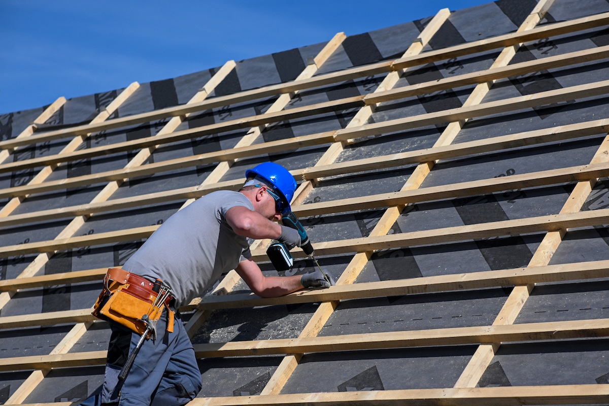 Repair and replacement of the old roof with a new one. Construction worker in protective clothing standing on roof with tools.
