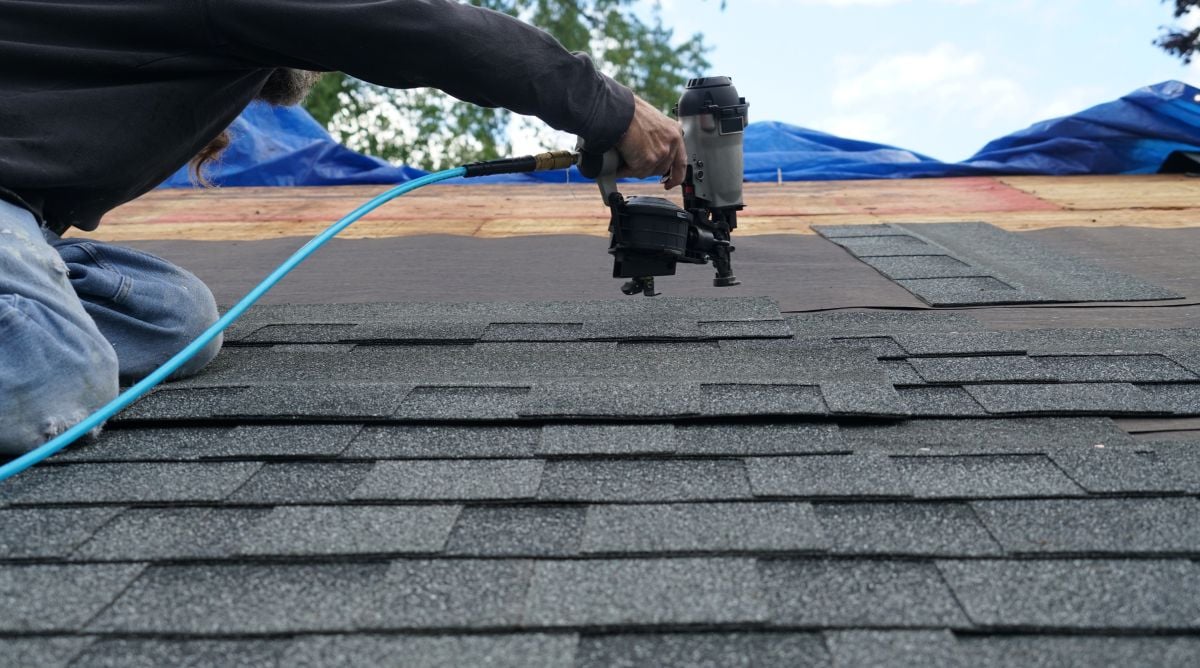 emergency roof tarping worker using nail gun to install shingle to repair roof