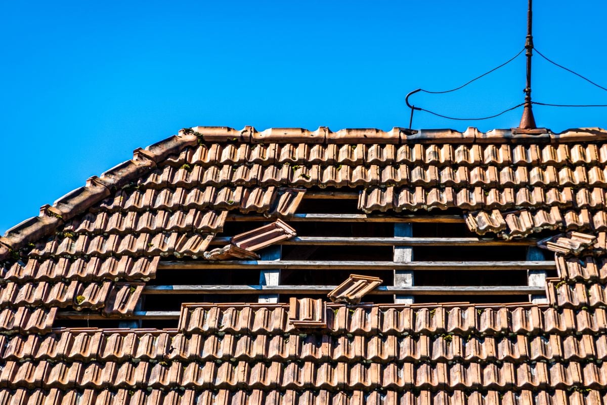 roof hail damage fallen ceramic tiles leaving a hole in old house blue sky